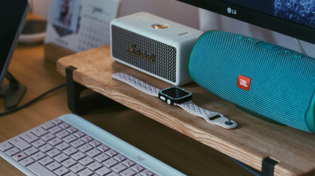 A close-up of a modern workspace featuring Bluetooth speakers, a smartwatch, and a keyboard.